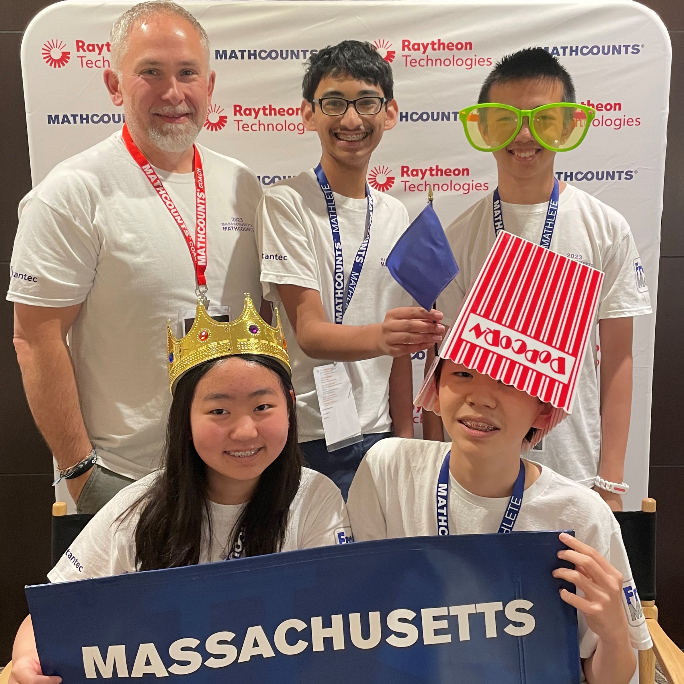 Massachusetts team (1 girl, 3 boys, and coach) smile with props and state team in front of photobooth backdrop.